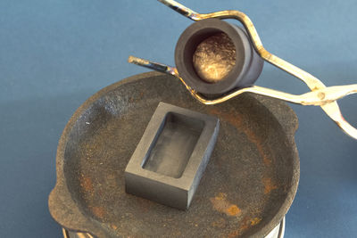 High angle view of melted metal being poured in container against blue background