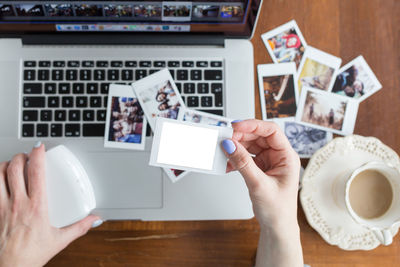 Cropped hand of woman holding photograph over laptop on table