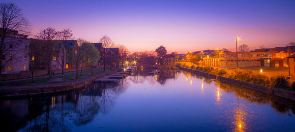 Illuminated bridge over river against sky at sunset