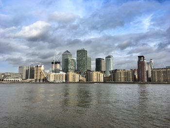 City at waterfront against cloudy sky