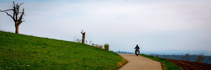 Rear view of people walking on road amidst field against sky