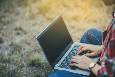 Midsection of man using laptop while sitting on field