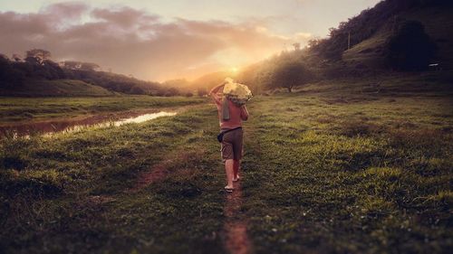 Rear view of man standing on field against sky during sunset