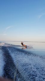 Young woman surfing on sea against blue sky