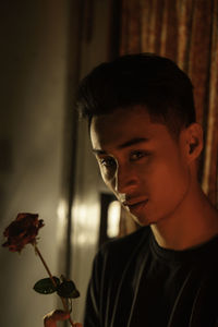 Close-up portrait of young man holding rose at home