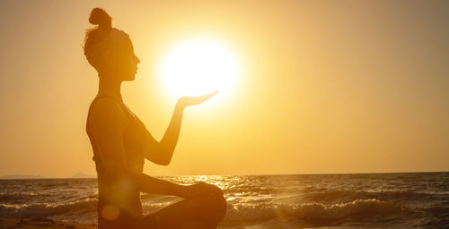 Side view of backlight and silhouette of young woman holding sun on the beach at sunrise or sunset