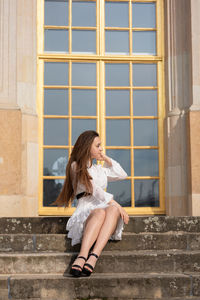 Full length of young woman sitting against window