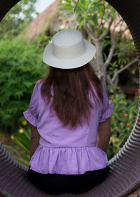 Rear view of woman wearing hat sitting outdoors