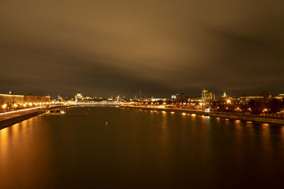 Illuminated city by river against sky at night