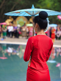 Rear view of woman in traditional clothing standing with umbrella by lake