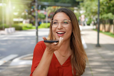 Brazilian student girl recording voice message on smartphone, talking with colleagues