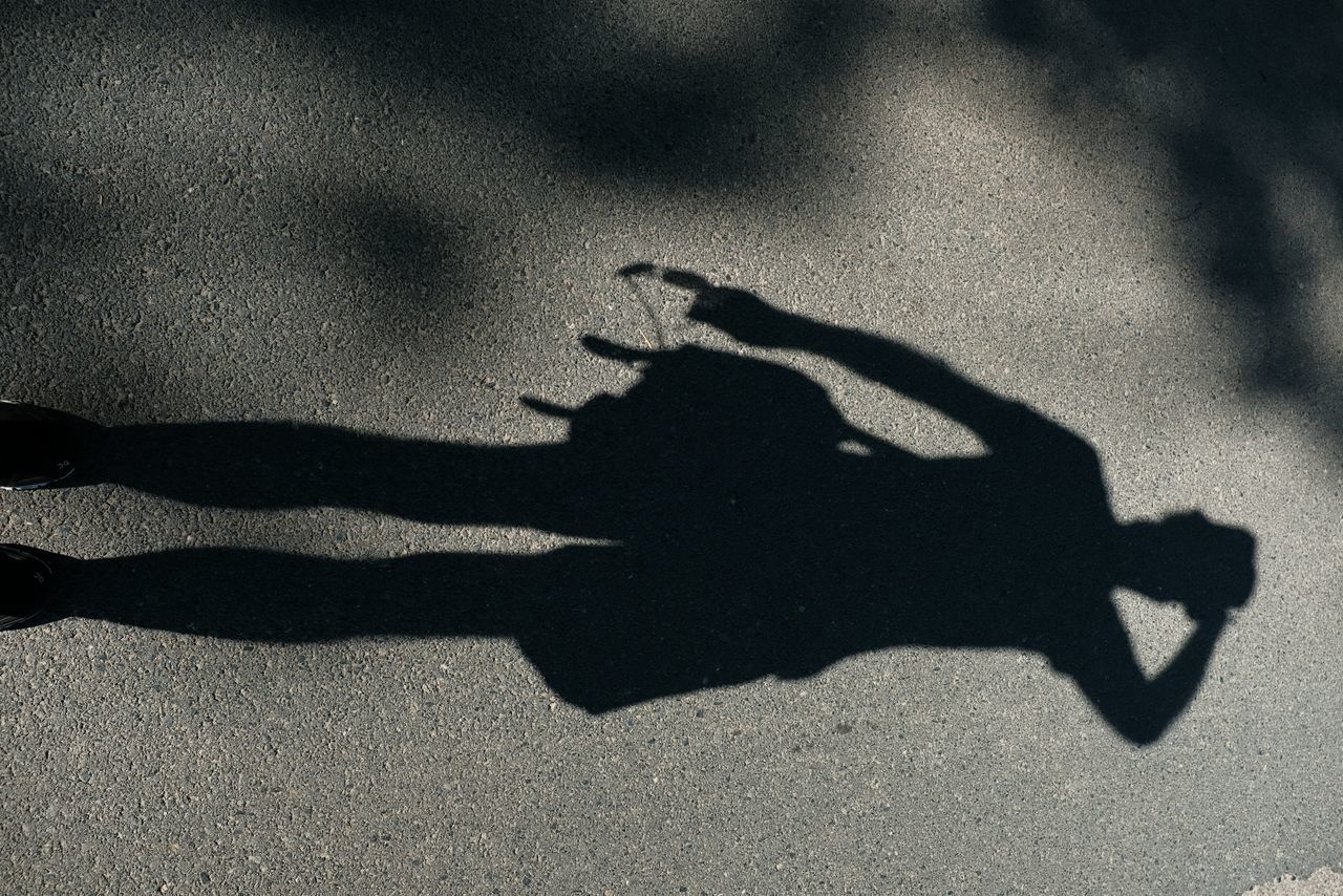 SHADOW OF MAN HOLDING UMBRELLA ON STREET