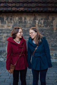 Smiling sisters standing against stone wall