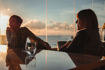 Women sitting on table at beach against sky