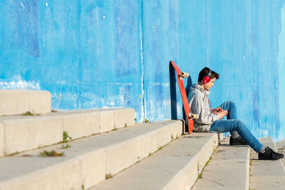 Teenager with headphones listening music while sitting on staircase.