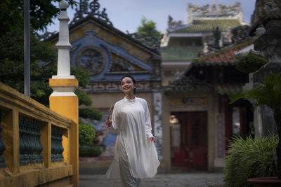 Portrait of young woman standing outside house against building