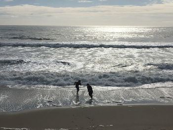 Silhouette people standing on beach against sky