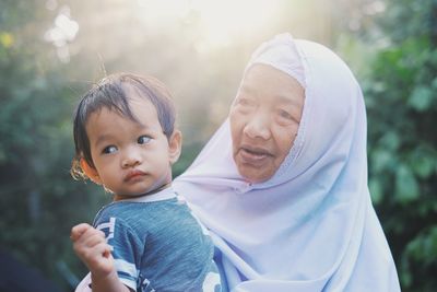 Close-up of grandmother carrying grandson against tree