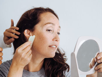 Middle age woman and cosmetologist making massage anti age procedures with guasha stone