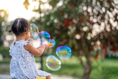 Cute little girl playing with soap bubbles at park.