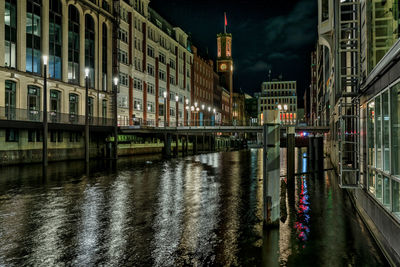 Illuminated bridge over canal by buildings in city at night