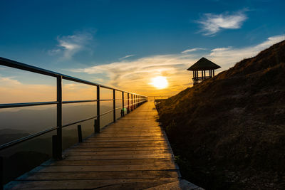 Footpath leading towards sea against sky during sunset