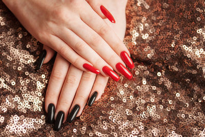 Hands of young girl with red and black manicure on nails on sequins background