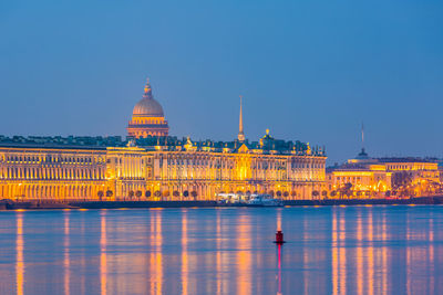 Illuminated building by river against sky in city
