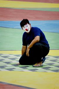 Full length of man with mask crouching on multicolored floor