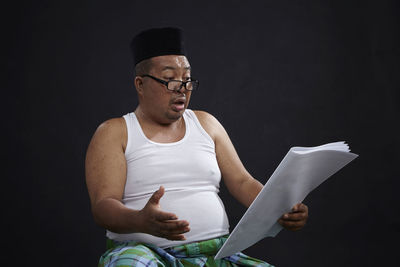 Man holding eyeglasses while sitting against black background