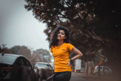 Portrait of woman standing by car against trees