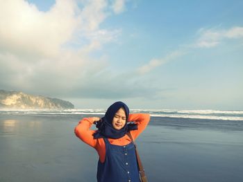 Young woman standing at beach against cloudy sky