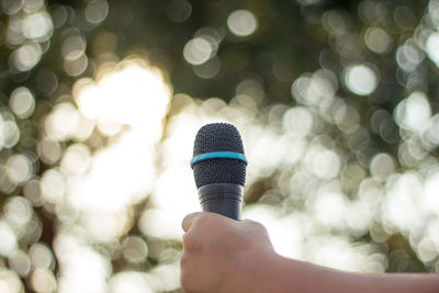 Cropped hand of person holding microphone against trees