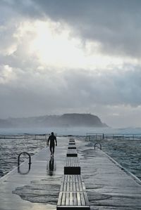 Man walking on pier amidst sea against cloudy sky