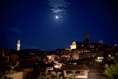 Illuminated buildings in town against sky at night