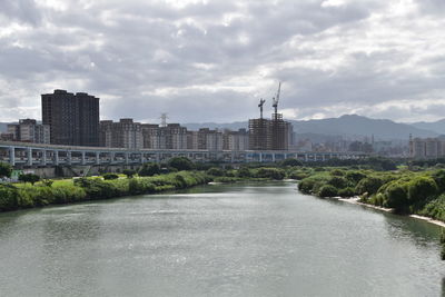 View of buildings by river against cloudy sky