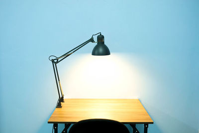 Illuminated lamp on table against wall