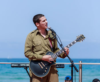 Full length of man playing guitar in sea against clear sky