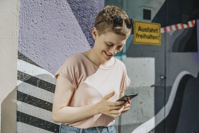 Mid adult woman text messaging on smart phone standing against colorful wall