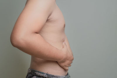 Midsection of shirtless woman against gray background