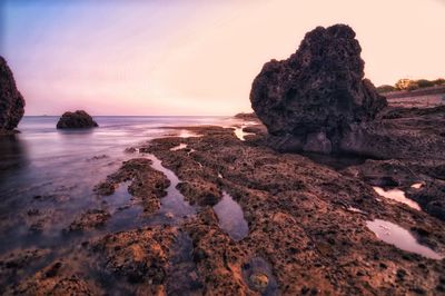 Rock formation on beach against sky during sunset