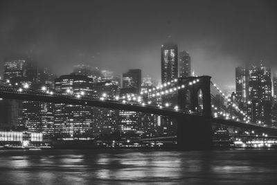 Illuminated buildings by river against sky in city at night