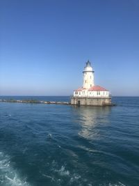 Lighthouse by sea against clear sky