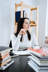 Female accountant working with many books and notepads on the background of laptop and calculator.