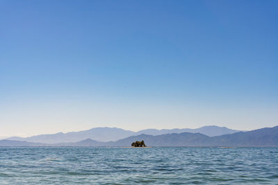 Scenic view of sea and island against clear blue sky