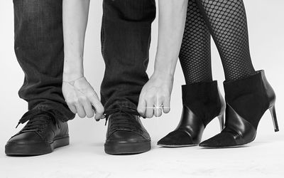 Low section man tying shoelace while standing by woman against white background