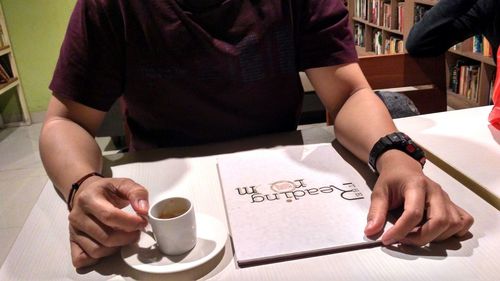 Midsection of man holding coffee cup on table