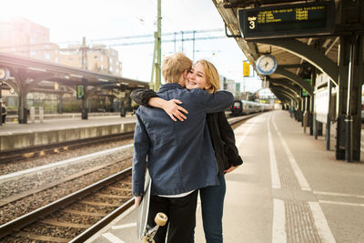 Young couple embracing while standing on railroad station platform