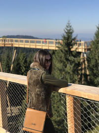 Woman standing by fence against sky