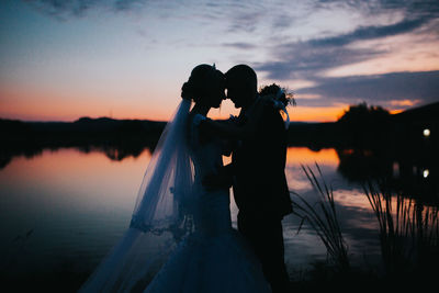 Couple kissing in lake against sky during sunset